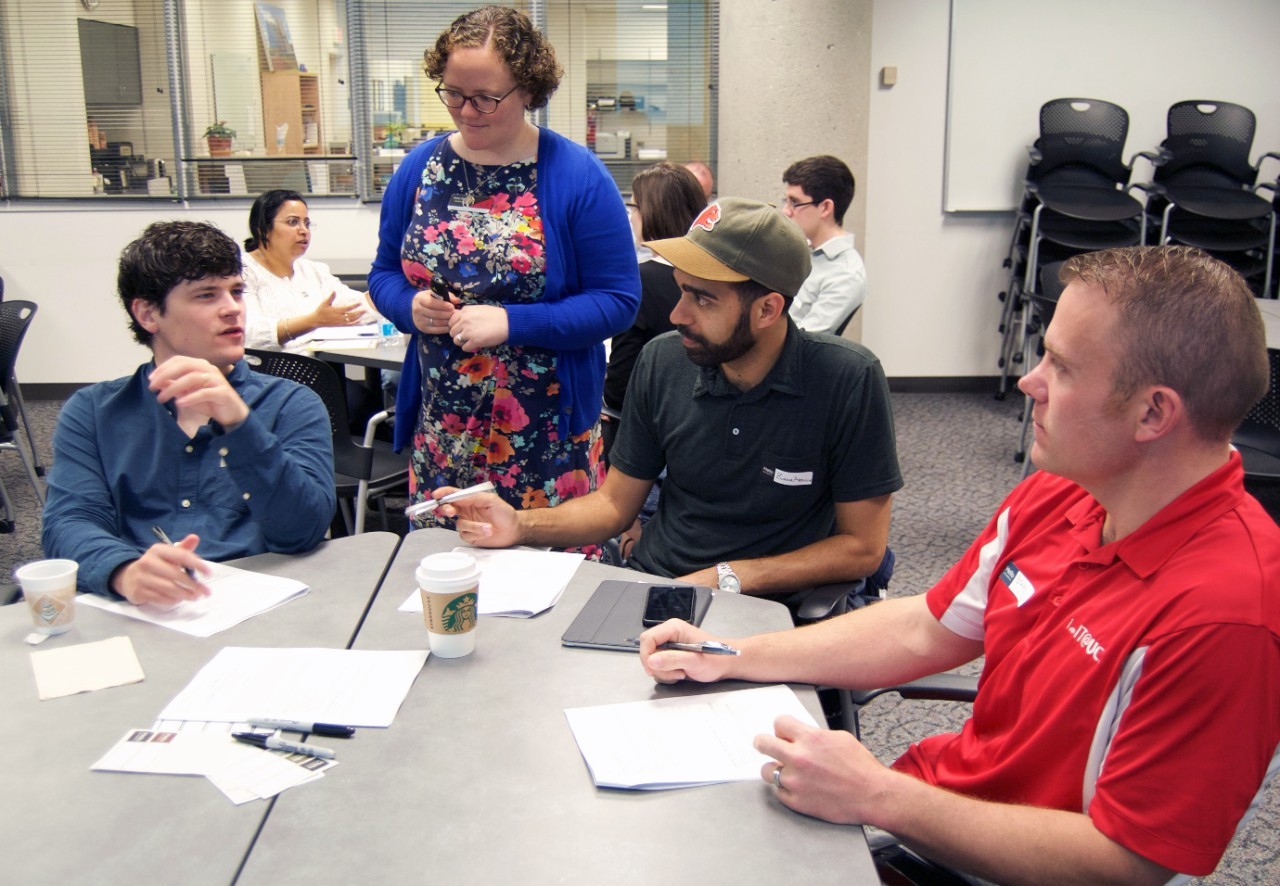 Graduate students sit at a round table and talk at a workshop.